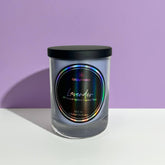 Glass candle with a black lid and colorful label on a white surface with a purple background