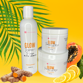 A set of skin care products including a bottle of body wash, a container of body scrub, and a tub of body butter, arranged with decorative elements like fruits and turmeric roots.